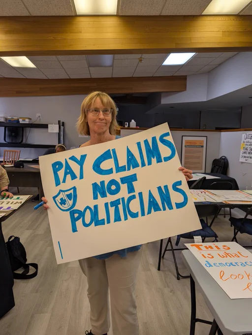 Holding a "Pay claims not politicians" sign