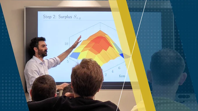 A person is giving a presentation using a slide that shows a 3D graph with colorful, triangular sections labeled "Step 2: Surplus S_{x,y}" on a large screen. Several people are seated and attentively watching in the foreground.