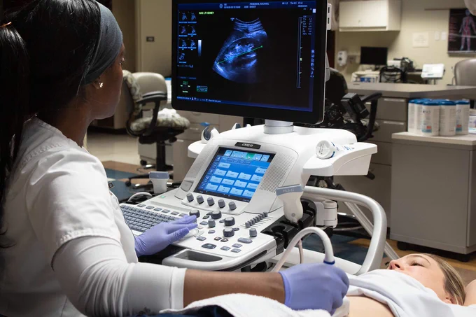 Female Chattanooga State student performing an abdominal ultrasound on a patient using advanced imaging equipment in the ChattState lab. Abdominal imaging on screen.