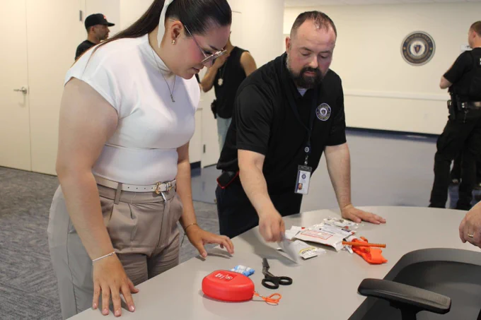 Two individuals examining emergency medical supplies, on a table in a training room.