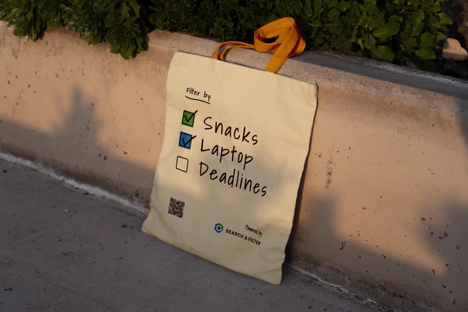 Mockup of the Search & Filter WCEU tote bag, design reads:

Filter by:
- [x] Snacks
- [x] Laptop
- [  ] Deadlines

Powered by Search & Filter