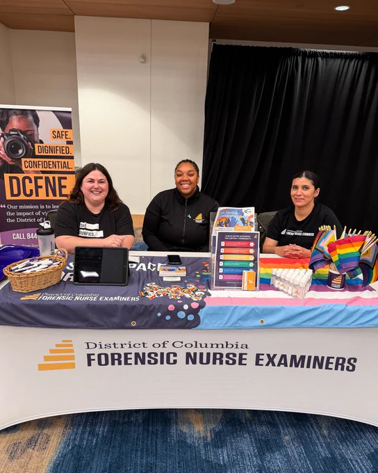 Members of DCFNE's outreach team pose at a table at DC's Black Trans Pride. On the table, there are Pride flags and stickers, as well as informational handouts about DCFNE's services for survivors of sexual assault and domestic violence. 