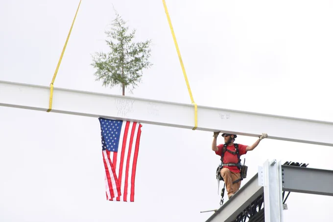 A construction worker steadies the ceremonial steel beam, decorated with an American flag and tree, during the topping out ceremony.