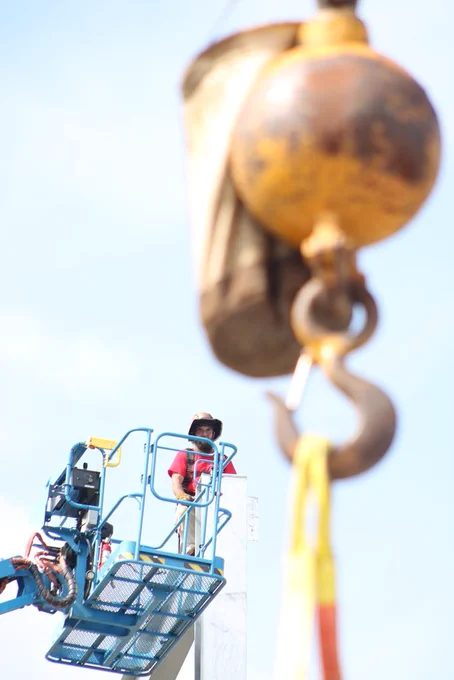 A construction worker stands in a lift near the crane hook as crews prepare to place the ceremonial beam at the Joe T. Robinson High School addition.