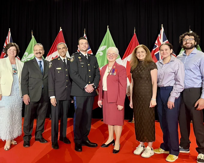 Paramedic Faez, distinguished guests, and loved ones standing on a stage with official flags in the background.