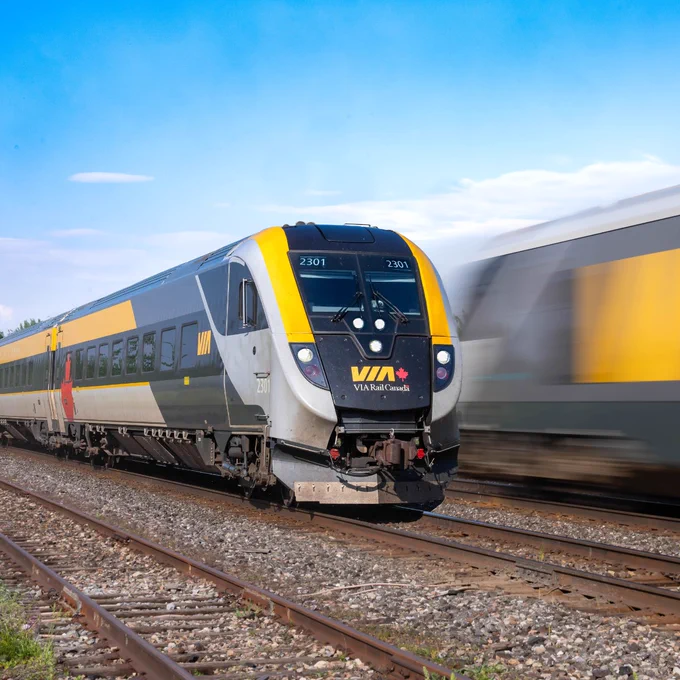 Train de VIA Rail sur des voies en milieu rural, avec un autre train passant rapidement en sens inverse.