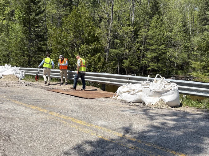 damage assessment crews walk along side road damaged by floodwaters