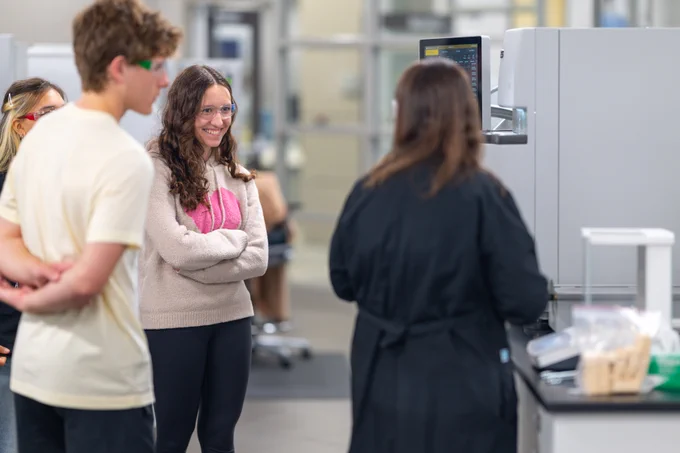 A group of students attentively watching a lab technician operate scientific equipment in a modern laboratory setting.