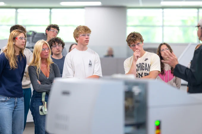 A group of young adults attentively listening to a presenter in a bright, modern classroom setting.