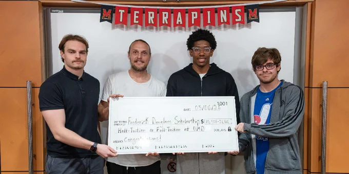Four students holding a large check for a Frederick Douglass Scholarship under a 'TERRAPINS' banner.
