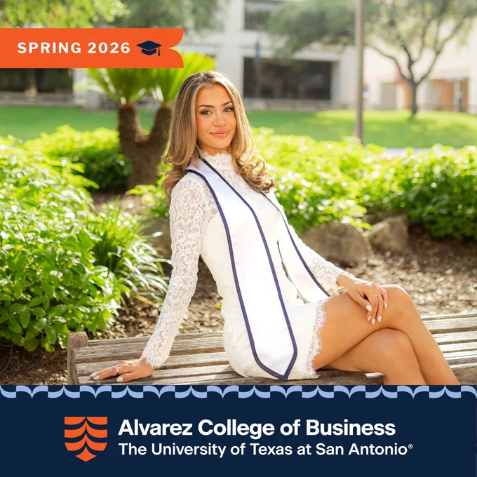 Mia Asturias in white lace dress and honor stole sitting on bench outdoors at University of Texas at San Antonio campus.