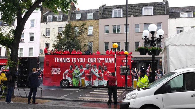 Arsenal men's football team celebrating 2015 FA cup win on a red bus with fans, thanking them for their support.