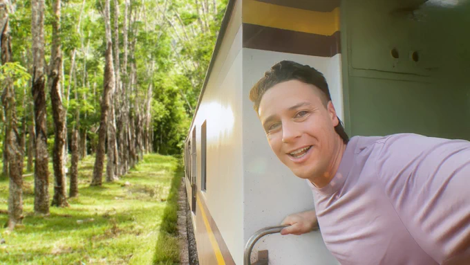 Michael Downie looks out over a sunlit forest from a train car.