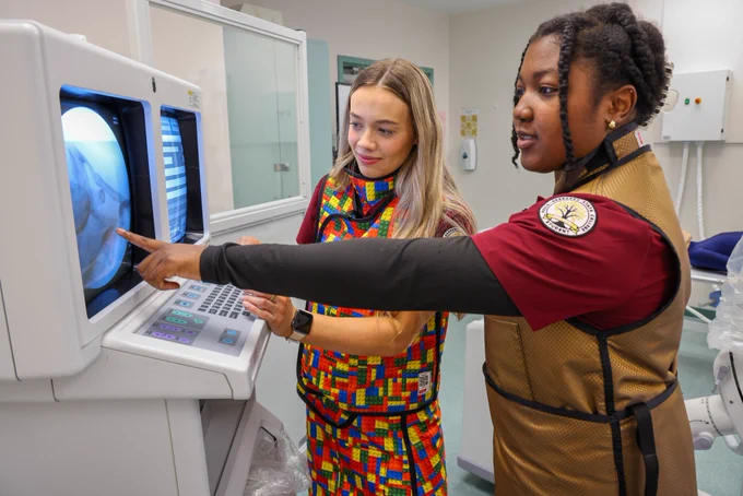 Radiography students pointing at X-ray lab equipment.