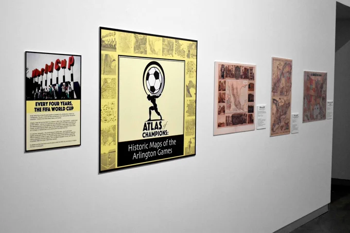 Pictured is a photo of historical maps and a sign for the Atlas of Champions exhibit that is on display at the Arlington Museum of Art.