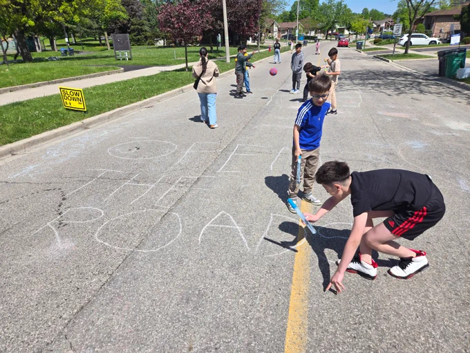 Children playing and drawing with chalk on a closed street during a sunny day in a suburban neighborhood.