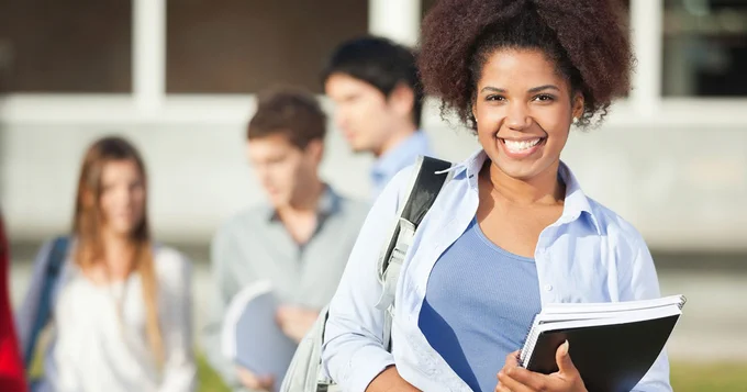 A person smiling while holding books and a backpack.