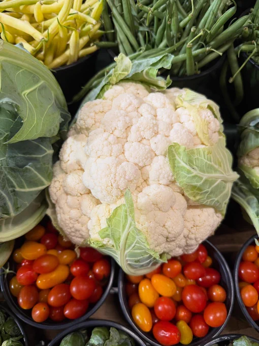 A large cauliflower surrounded by fresh green beans and small red and orange tomatoes.