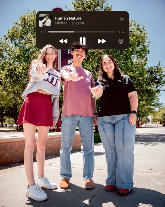 Three people standing outdoors, smiling and reaching out towards the camera. A music player overlay shows "Human Nature" by Michael Jackson. Trees and a campus background are visible.