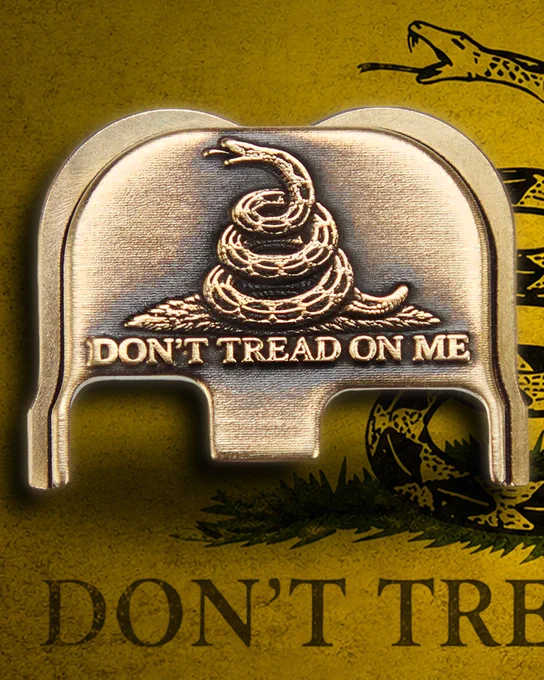 Close-up of a pistol featuring a brass “Don’t Tread On Me” engraved rear slide plate against a yellow Gadsden flag background with a coiled rattlesnake graphic.