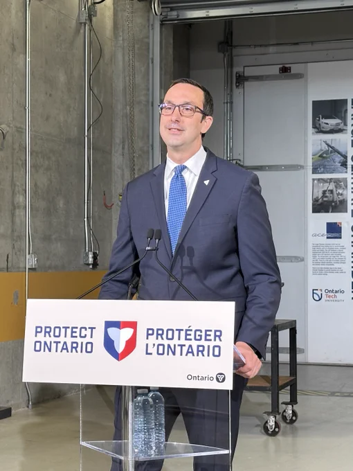 Hon. Nolan Quinn, Minister of Colleges, Universities, Research Excellence and Security (MCURES) stands at a podium with a sign that says "Protect Ontario" as he delivers remarks inside Ontario Tech's ACE facility.
