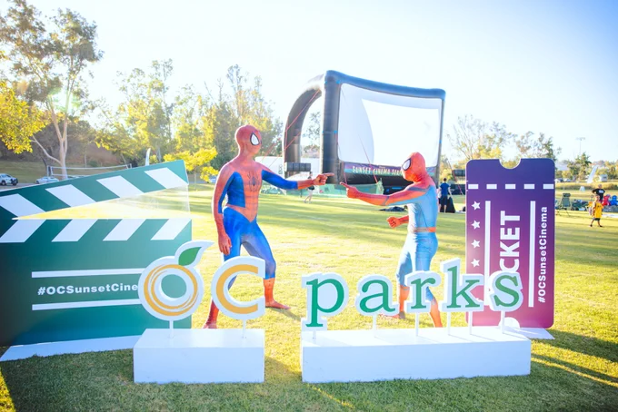 OC Parks sign with two costumed Spiderman in front of a movie screen.