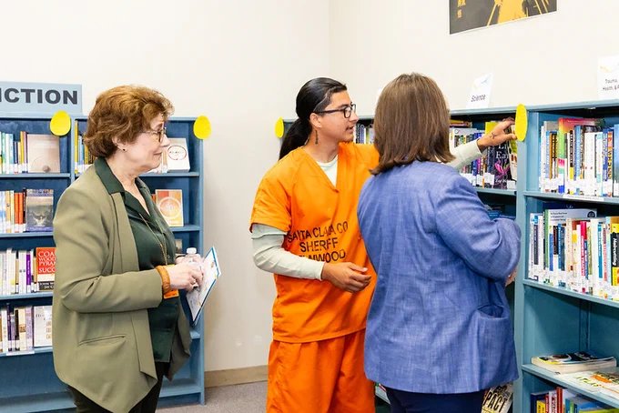Incarcerated person looks at books alongside visitors of the new library.
