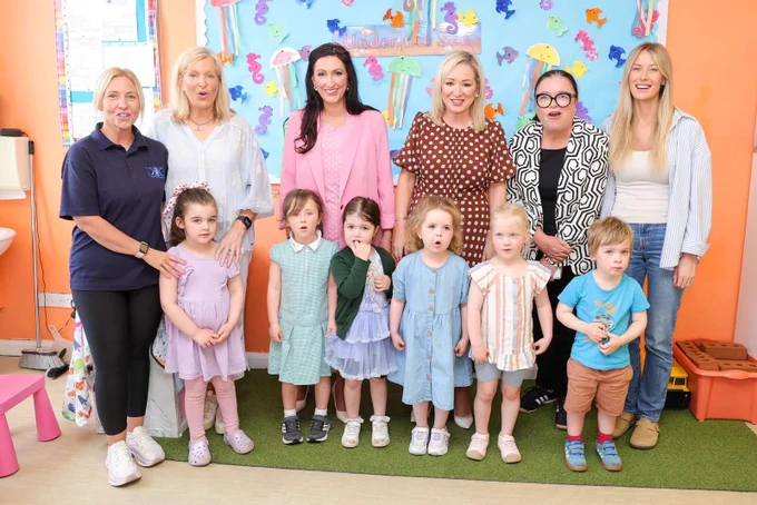 Image of 12 people standing – First Minister Michelle O’Neill and deputy First Minister Emma Little-Pengelly pictured with children and staff during their visit to Kids Korner Day Nursery in Belfast.