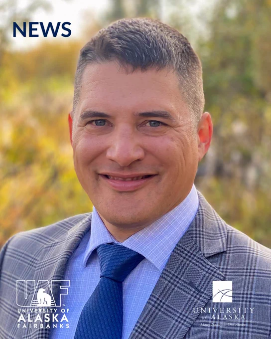 A man in a gray plaid suit, light blue shirt, and blue tie smiles warmly in a portrait. The background is a blurred outdoor scene with trees. The words "NEWS" appear in the top left corner. Logos for the University of Alaska Fairbanks and the University of Alaska are in the lower corners.