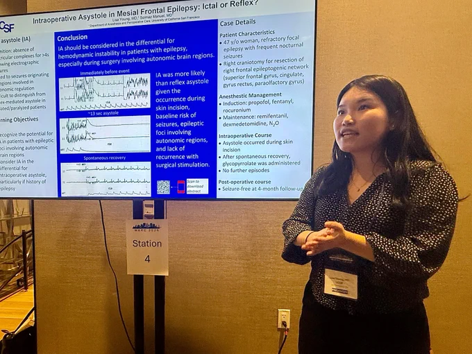 A woman standing by a scientific poster entitled, "Intraoperative Asystole in Mesial Frontal Epilepsy: Ictal of Reflex?"