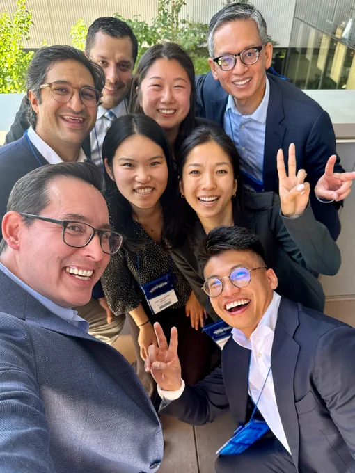A group of eight people wearing suite and name-tags posing together for a selfie.