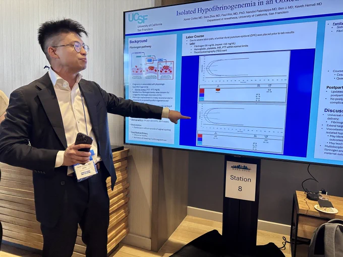 A man wearing a dark suit standing by a scientific poster and pointing at a graph on the poster.