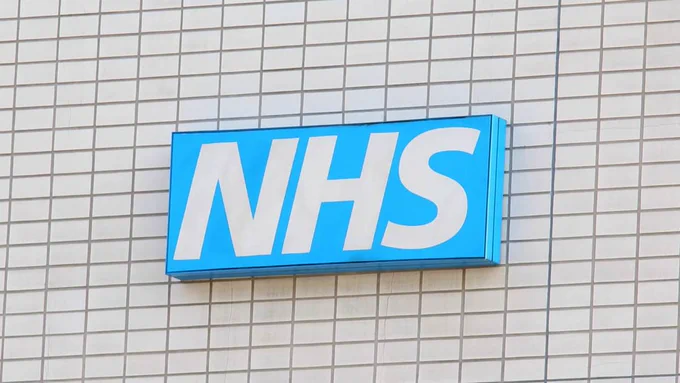 Blue NHS logo sign on a light tiled wall, representing England’s National Health Service.
