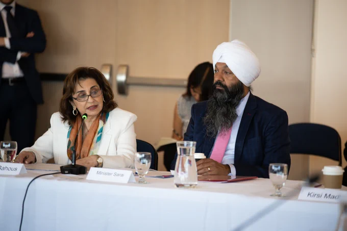 UN Women Executive Director Sima Bahous is speaking into a mic, seated at a table next to Secretary of State Randeep Sarai.