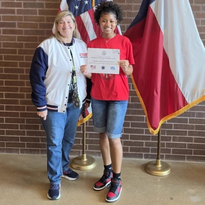 Photo of Principal Dr. Arredondo and Michelle posing with the Certificate of Appreciation in front of the U.S. and Texas flags.