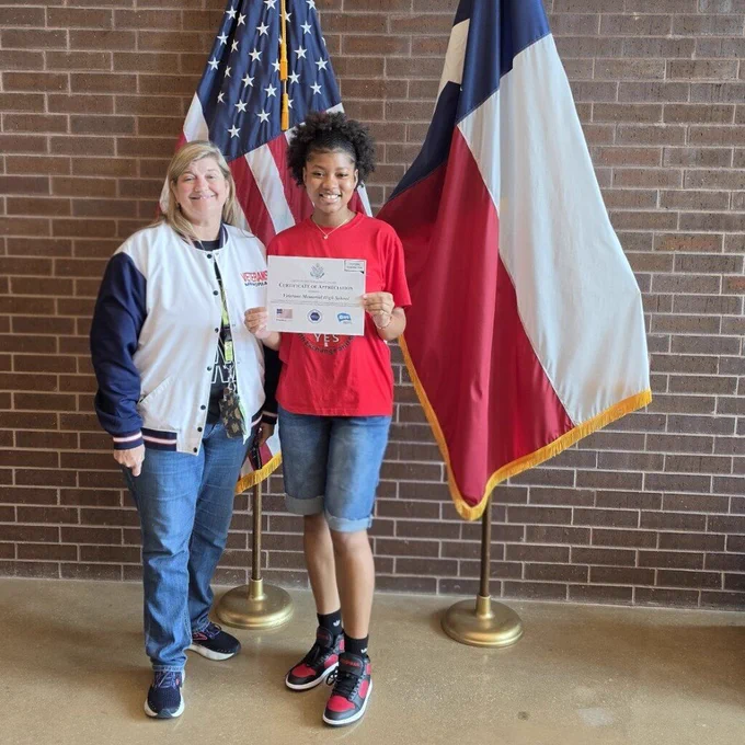 Photo of Principal Dr. Arredondo and Michelle posing with the Certificate of Appreciation in front of the U.S. and Texas flags.