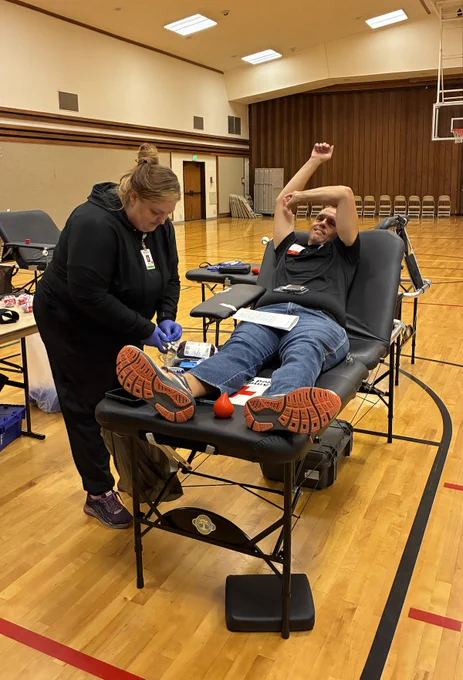 Man on a table, stretching, while a phlebotomist prepares for a blood donation