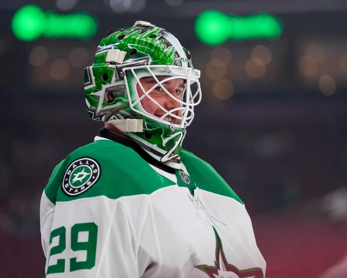 Jake Oettinger smiling while wearing a white away Stars jersey and goalie mask 