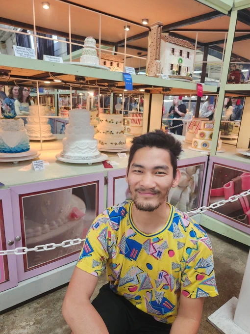 A middle-aged Asian man kneeling in front of a display of cakes at the N.C. State Fair. 