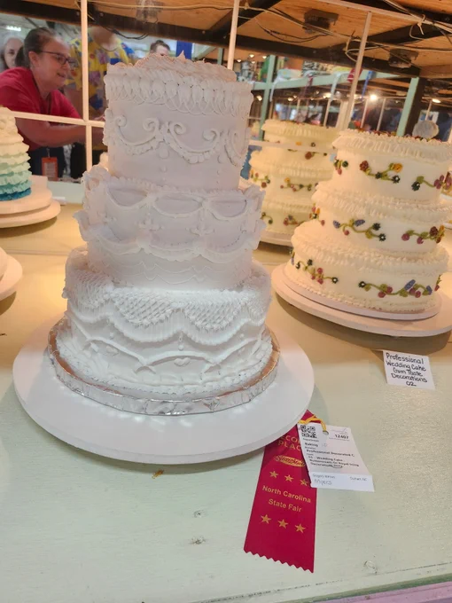 A cake inside a glass display with a red second-place ribbon laying next to it. 