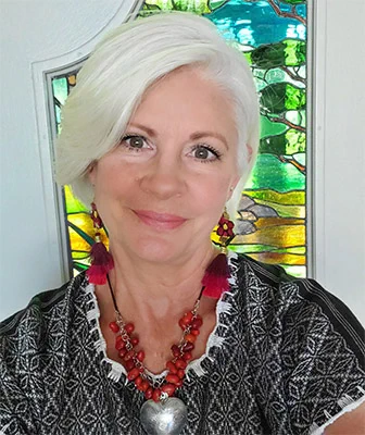 A person posed and smiling in front of a green glass window.