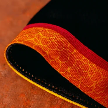 Close-up of a corner of a book with a decorative edge, featuring intricate yellow and red patterns, set against a textured orange surface.