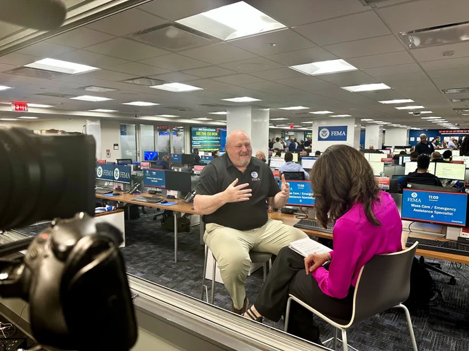 Senior Official Performing the Duties of Administrator Bob Fenton in a black polo shirt is interviewed by Nicole Sganga in a pink blouse inside the NRCC.