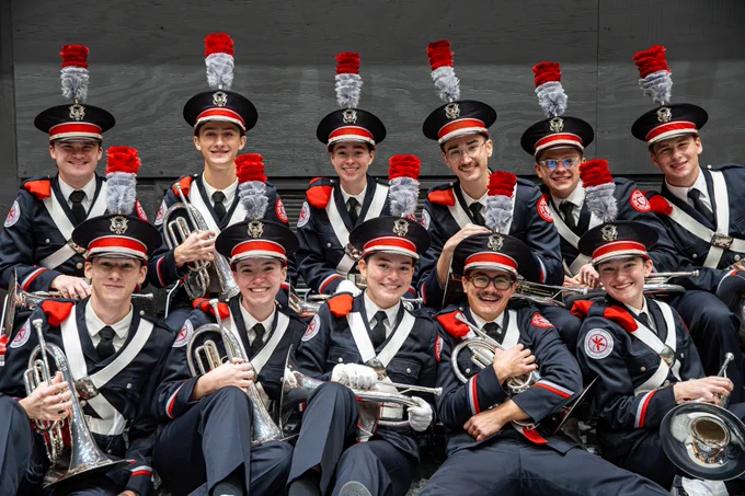A group of students in marching band uniforms, holding mellophones, pose for a photo.