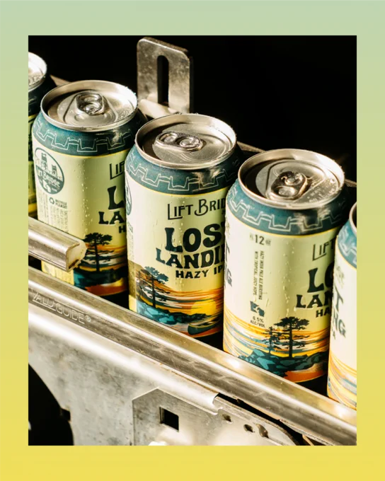 Close-up of Lift Bridge's Lost Landing Hazy IPA cans in a production line. The scene is well-lit, showcasing the vibrant design of the cans.