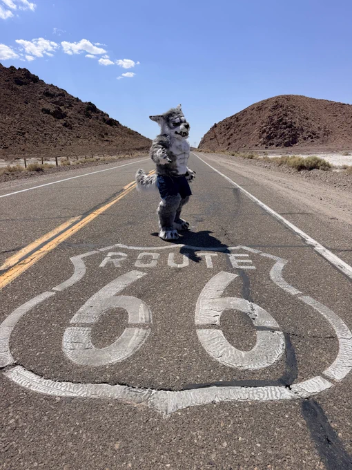 Cray the Werewolf is wearing just the torn jean shorts and one clawed hand stretched out while standing on an open paved road with a large "ROUTE 66" highway shield painted on the road surface.