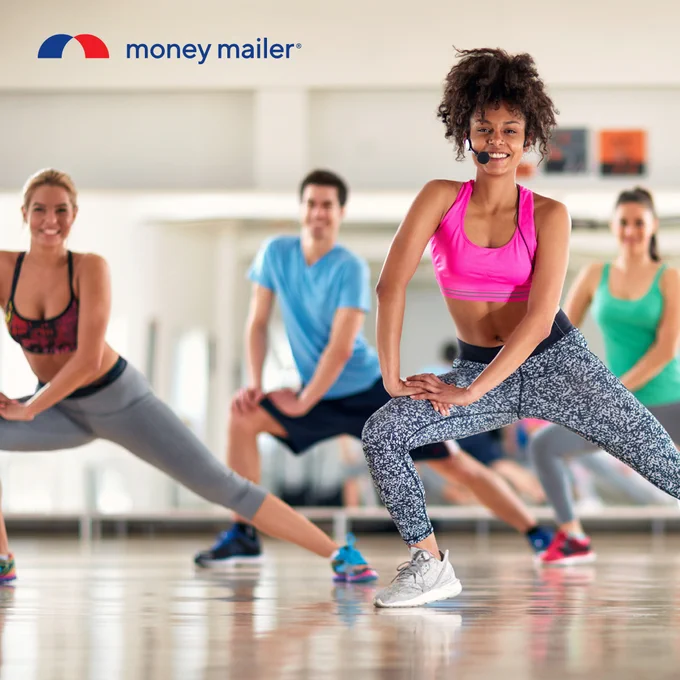 Group of diverse adults performing side lunges during a fitness class in a bright studio with wooden floors.