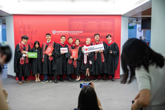 Group of graduates posing for photos in the regalia while holding HKS graduation props.