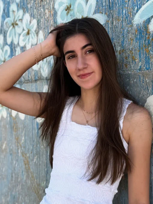 Isabella Schlick leans against a cement wall while wearing a white top