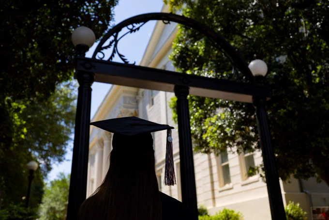 A person in a graduation cap stands in front of the Arch, a historic monument at the University of Georgia. 